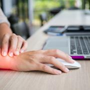 A hand on a mouse next to a computer with glowing red light on the wrist showing wrist pain